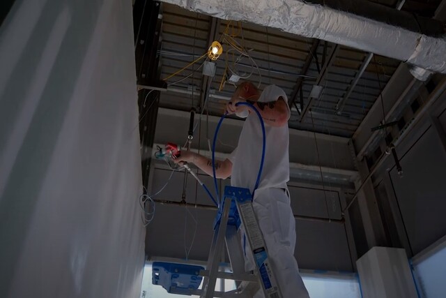 Worker commercial painting an interior building wall on a ladder